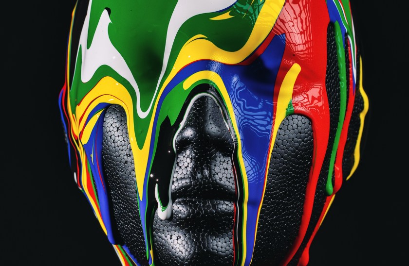 Close-up of a black mannequin head covered in glossy, multicolored paint dripping downward against a dark background.