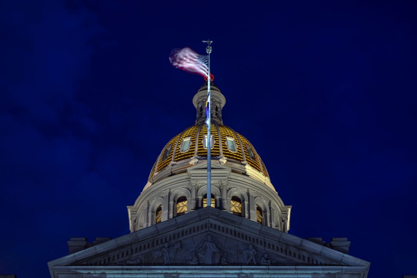 Night view of the Colorado State Capitol dome with a motion-blurred American flag against a deep blue sky.
