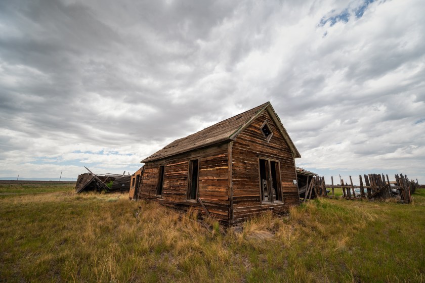 Weathered wooden house with broken windows standing alone in grassland under an overcast sky in Bosler, Wyoming.