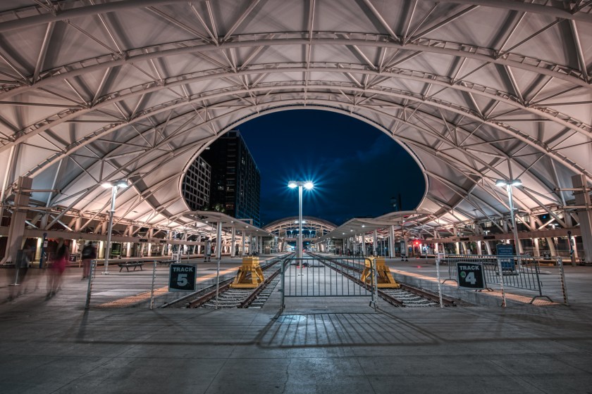Symmetrical view of covered light rail platforms inside Denver Union Station at night, with tracks centered beneath a white arched roof.