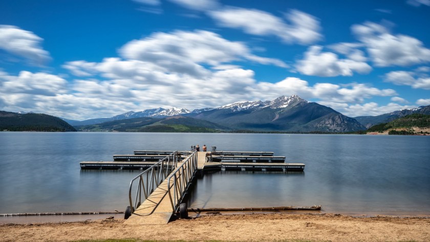 Long exposure view of a dock extending into Dillon Reservoir with mountains and blurred clouds in the background.