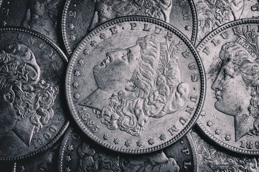 Close-up photograph of overlapping Morgan silver dollar coins showing worn engraved profiles and inscriptions.
