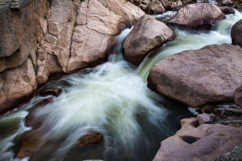 Long exposure view of a small waterfall flowing through smooth granite boulders along St. Vrain Creek.
